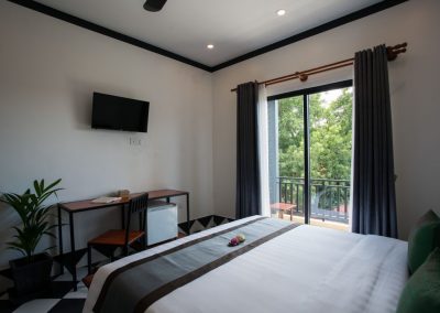 Modern hostel room featuring a king-size bed, work desk, flat-screen tv, and private balcony.